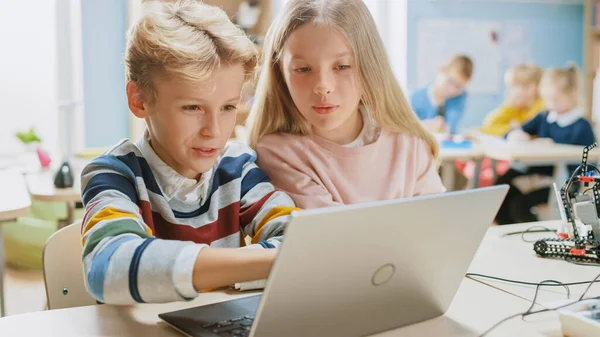 Brillante colegiala y colegial hablan y utilizan el ordenador portátil para programar software para la clase de ingeniería de robótica. Aula de Ciencias de la Escuela Primaria con Niños que Trabajan en Tecnología. Educación STEM —  Fotos de Stock