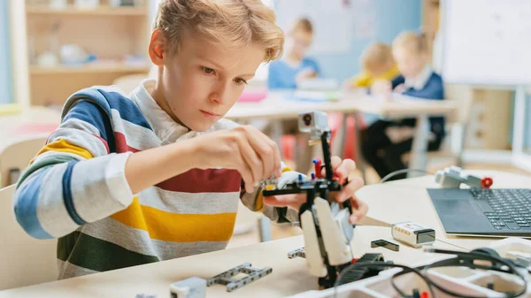 Schoolboy costruisce piccoli robot e utilizza il computer portatile per programmare il software per la classe di ingegneria robotica. Scuola Elementare Science Classroom con i bambini brillanti dotati che lavorano con la tecnologia — Foto Stock