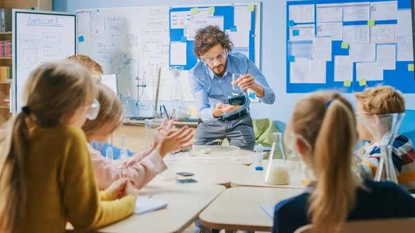 Elementary School Chemistry Classroom: Enthusiastic Teacher Teaches Group of Children, Shows Science Experiment by Mixing Chemicals in the Beaker (en inglés). Niños recibiendo educación moderna, aprendiendo cosas nuevas —  Fotos de Stock