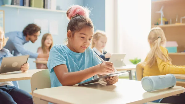 Elementary School Computer Science Class: Cute Girl utiliza Tablet Computer digital, sus compañeros de clase también trabajan con computadoras portátiles. Niños recibiendo educación moderna en STEM, jugando y aprendiendo — Foto de Stock
