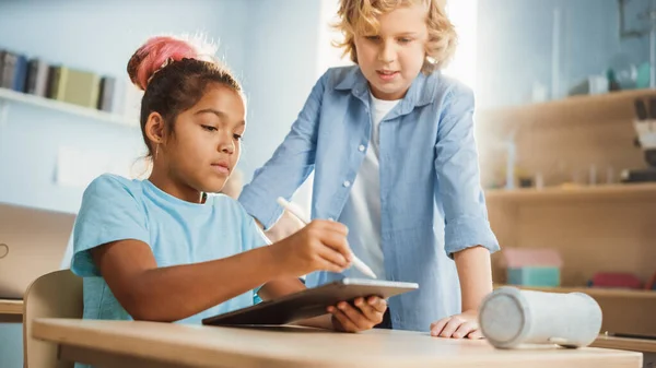 小学校コンピュータサイエンスクラス:スマートガールは、デジタルタブレットコンピュータを使用しています,彼女のクラスメイトは、割り当てで彼女を助けます.近代教育を受ける子供たち — ストック写真