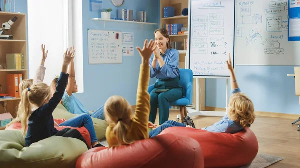 Basisschool Creativiteit klasse: Kinderen zitten op de Bonentassen met opgeheven handen met antwoord. Leraar verklaart Les en Vraagt Vragen. Leren in een moderne omgeving. — Stockfoto