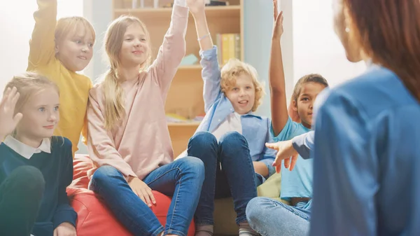 Elementary School Creativity Class: Children Sitting on the Bean Bags while Teacher Explains Lesson and Asks Question, Every Child Raises Hand with Answer. Learning in Modern Environment. — Stock Photo, Image