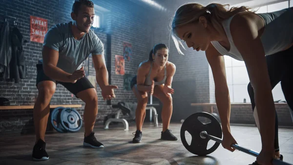 Male and Female Fitness Trainers Encourage a Beautiful Fit Athletic Young Woman in Her Daily Workout. She is Successfully Lifting a Heavy Barbell. Training is Held in a Gym with Motivational Posters. — Stock Photo, Image