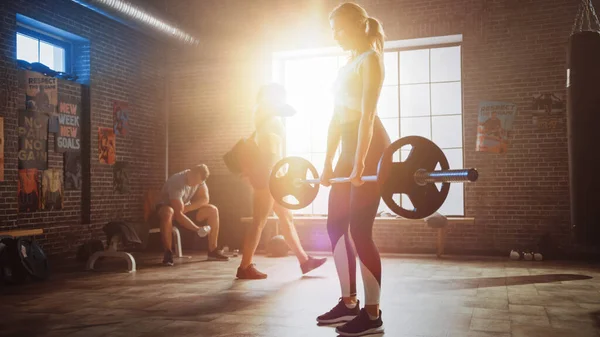 Die schöne fitte athletische Blondine hebt eine Langhantel vom Boden und macht rückenstärkende Übungen als ihre tägliche Fitness-Trainingsprogramme. Fitnessstudios im Loft mit warmer Sonneneinstrahlung. — Stockfoto