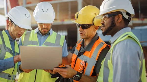 Une équipe diversifiée de spécialistes utilise un ordinateur portable sur le chantier de construction. Projet de construction immobilière avec un ingénieur civil, un investisseur en architecture, une femme d'affaires et un travailleur discutant du plan directeur — Photo