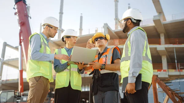 Equipo Diverso de Especialistas Utilice Computadora Portátil en el Sitio de Construcción. Proyecto de construcción inmobiliaria con maquinaria: Ingeniero civil, inversor, mujer de negocios y constructor discutiendo el plan Blueprint —  Fotos de Stock