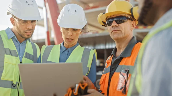 Une équipe diversifiée de spécialistes utilise un ordinateur portable sur le chantier de construction. Projet de construction immobilière avec des machines : Ingénieur civil, investisseur, femme d'affaires et constructeur discutant du plan directeur — Photo