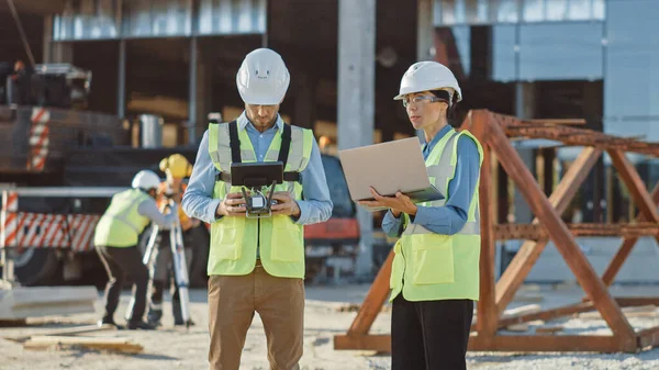 Dos especialistas controlando drones en un sitio de construcción. Ingeniero de arquitectura e inspector de ingeniería de seguridad vuelan dron en construcción de edificios comerciales sitio de control de diseño y calidad —  Fotos de Stock