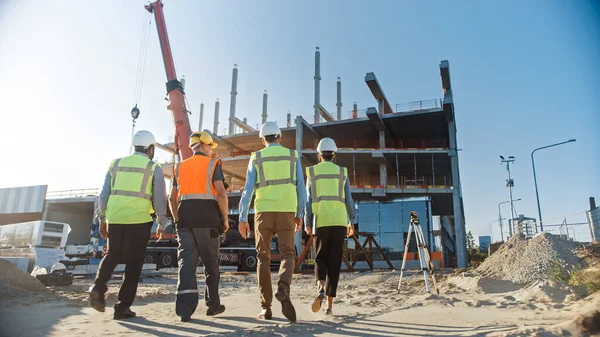 Equipo Diverso de Especialistas Inspeccionan el Sitio Comercial de Construcción de Edificios Industriales. Proyecto inmobiliario con Ingeniero Civil, Inversionista y Trabajador. En la grúa de fondo, marcos de encofrado de rascacielos —  Fotos de Stock