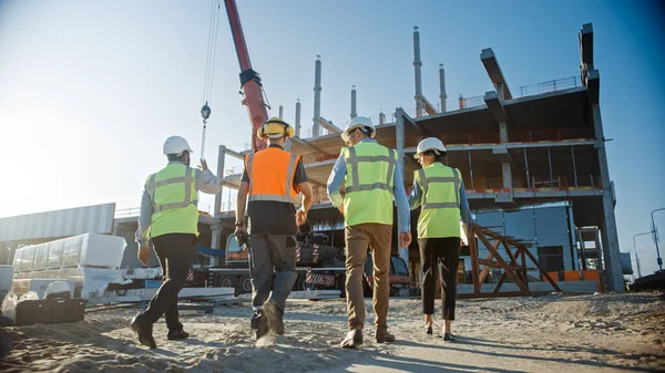 Equipo Diverso de Especialistas Inspeccionan el Sitio Comercial de Construcción de Edificios Industriales. Proyecto inmobiliario con Ingeniero Civil, Inversionista y Trabajador. En la grúa de fondo, marcos de encofrado de rascacielos — Foto de Stock