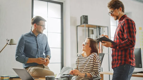 Jovem mulher e dois colegas masculinos tendo uma reunião amigável e discutindo novas ideias de negócios. Ambiente de Coworking Easygoing em Loft Office Creative Agency. Eles fazem anotações no laptop e tablet . — Fotografia de Stock