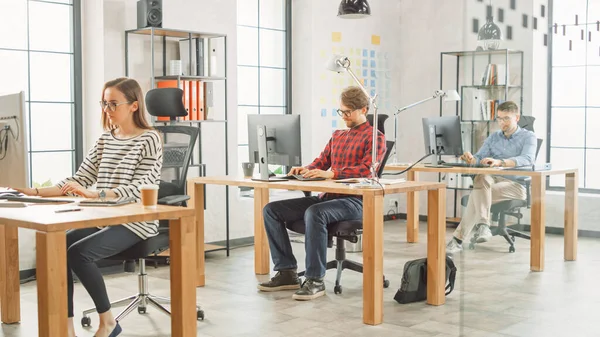 Shot of Creative Agency Life. Female Colleague Works with two Male Coworker Behind Desks. Creative Office Concept. They Work on Computers and Laptops.