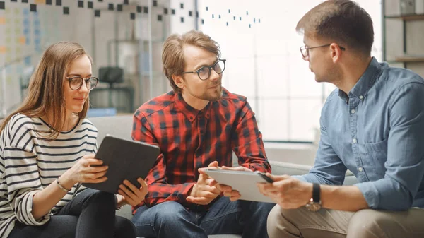 Young Woman and Two Male Colleagues Having a Friendly Meeting and Discussing New Business Ideas. Easygoing Coworking Atmosphere in Loft Office Creative Agency. They Look at Papers and Tablet. — Stock Photo, Image