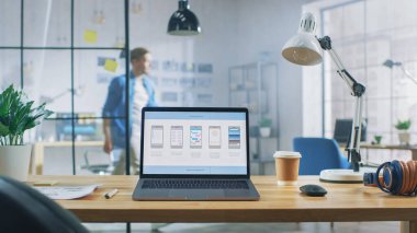 Ofisteki masadaki dizüstü bilgisayar Mobil Telefon Uygulama Tasarımı, Yazılım UI Geliştirme ile Ekranı gösterir. Arkaplanda Modern Açık Alan Ofisi HUB ile Profesyonel Çalışma