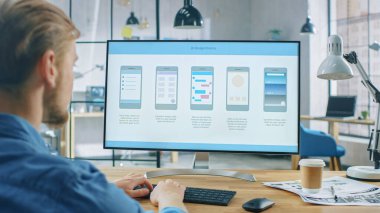 Yaratıcı Ofis 'teki Masasında Genç Profesyonel Bilgisayar Çalışmaları. Monitör Ekranı Cep Telefonu Uygulama Tasarımı, Yazılım UI Geliştirmesini gösterir. Arkaplanda Yaratıcı Modern Ofis