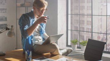 Proje üzerinde çalışırken Profesyonel Yaratıcı Tasarımcı Dizüstü bilgisayarının üzerinde oturur dizlerinin üzerinde Sabah Kahvesini içer. Yaratıcı Tasarım ve Oyun İçeriği Geliştirme Stüdyosu