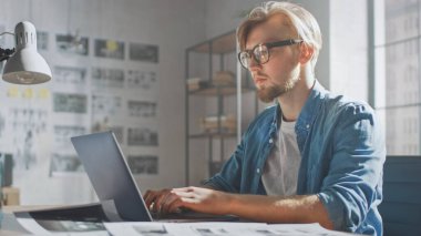 Yaratıcı Tasarımcı, Modern Stüdyoda Masasında Oturan Dizüstü Bilgisayarını kullanarak, Bir Storyboard, Duvarda Asılı Taslak ve Konseptler Projesi üzerinde çalışıyor. Video Düzenleme, Uygulama UI veya Oyun Çizimi