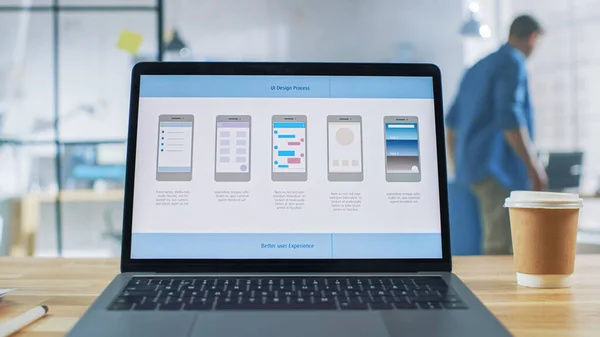 Ноутбук на столі в екрані Office Show з дизайном додатків для мобільних телефонів, розробкою програмного інтерфейсу. На задньому плані Creative Modern Open Space Office HUB з професійною роботою — стокове фото