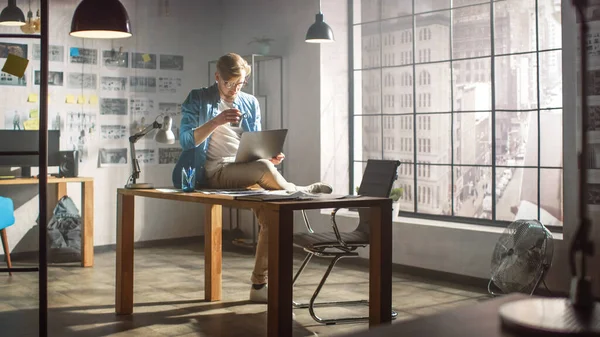 在该项目的工作中，专业创意设计师坐在膝盖上的台架笔记本电脑上，一边喝早茶。创意设计及游戏内容开发工作室 — 图库照片