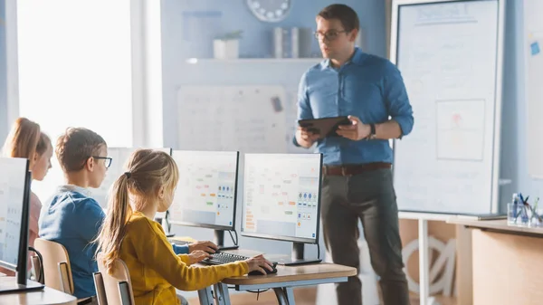 Classe de l'école primaire : L'enseignant utilise un tableau blanc numérique interactif, explique la leçon à un groupe diversifié d'enfants intelligents. Les enfants reçoivent une éducation moderne, apprennent l'informatique, programment des logiciels — Photo