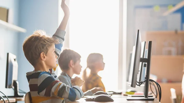 Elementary School Science Classroom: Boy raise hand with question (en inglés). Profesor educa a los pequeños escolares inteligentes que trabajan en computadoras personales, aprenden lenguaje de programación para la codificación de software. — Foto de Stock