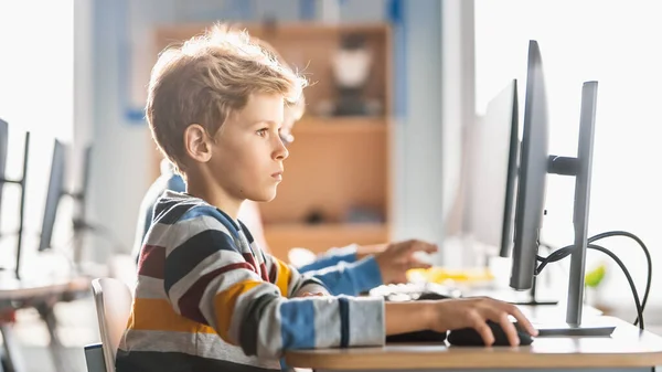 Scuola elementare aula di Informatica: Ragazzino carino utilizza Personal Computer, Linguaggio di programmazione di apprendimento per la codifica del software. Studenti che ricevono un'educazione moderna. Ritratto vista laterale — Foto Stock