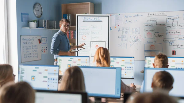 Grundschulklasse: Lehrer verwendet interaktives digitales Whiteboard, erklärt verschiedenen Gruppen intelligenter Kinder den Unterricht. Kinder erhalten moderne Bildung, lernen Informatik, Softwareprogrammierung — Stockfoto