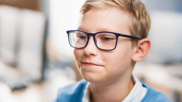 Porträtt av en söt liten pojke klädd glasögon, sitter vid sin skolbänk, ler lyckligt. Smart liten pojke med charmigt leende som sitter i klassrummet. Närbild Porträtt Skott — Stockfoto