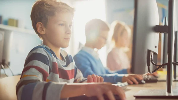 Aula de la escuela primaria: Boy utiliza la computadora personal, aprendiendo cómo utilizar Internet de forma segura, lenguaje de programación para la codificación de software. Los escolares reciben educación moderna. Filmado con filtro caliente —  Fotos de Stock