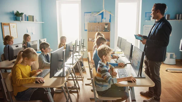 Escuela Primaria de Ciencias de la Computación Aula: Profesor utiliza Tablet Computer, Explica Lección a Diverso Grupo de Niños Inteligentes. Clase de informática Niños aprenden: Seguridad en Internet, Programación de software —  Fotos de Stock