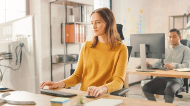 Güzel ve zeki kızıl saçlı kadın uzmanı masasında oturuyor. Masaüstü bilgisayarında çalışıyor. Gelişen Başlangıç İçin Çalışan Profesyonellerin Çeşitli Grubu ile Arka plan Modern Parlak Ofisinde