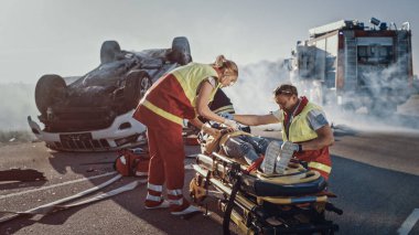 Trafik kazası sahnesinde, sedyelerin üzerinde yatan küçük bir kızın hayatını kurtaran sağlık görevlileri, ilk yardım aldı. İtfaiyeci Ana 'yı Kızına Götürdü. Arkaplanda Takla Aracı