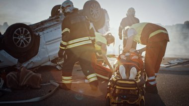 Trafik kazası sahnesinde, itfaiyecilerden oluşan kurtarma ekibi, kadın kurbanı araçtan çıkardı, sedyeyi dikkatle kullandılar, ilk yardım yapan sağlık görevlilerine teslim ettiler.