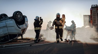 Cesur İtfaiyeci Yaralı Genç Kızı Sevgi dolu annesine kavuştuğu güvenli bir yere taşıyor. Arkaplan Kazasında Trafik Kazasında Cesur Sağlık Görevlileri ve İtfaiyeciler Hayat Kurtarıyor
