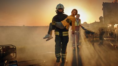 Cesur İtfaiyeci Yaralı Genç Kızı Sevgi dolu annesine kavuştuğu güvenli bir yere taşıyor. Arkaplan Kazasında Trafik Kazasında Cesur Sağlık Görevlileri ve İtfaiyeciler Hayat Kurtarıyor