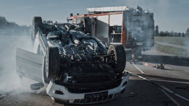 Trafik Kazası Sigara İçen ve Yanan Araç Çarpışmadan Sonra Yolun Ortasında Çatısında Yatıyor. İtfaiye ve itfaiye araçlarından oluşan bir ekipte. Düşük Karşıtlık