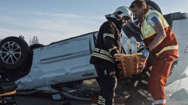 Trafik kazası sahnesinde, itfaiyecilerden oluşan kurtarma ekibi, kadın kurbanı araçtan çıkardı, sedyeyi dikkatle kullandılar, ilk yardım yapan sağlık görevlilerine teslim ettiler.