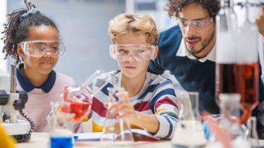 İlköğretim Okulu Bilim Sınıfı: Coşkulu Öğretmen Kimya ile Çeşitli Çocuklar Grubuna Yardım Ediyor, Küçük Çocuk Bemicals 'ı Beakers' a Karıştırıyor. Çocuklar Faiziyle Öğrenin