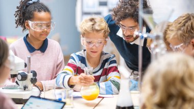 İlköğretim Okulu Bilim Sınıfı: Coşkulu Öğretmen Kimyayı Çeşitli Çocuklar Grubu 'na Açıkladı, Küçük Çocuk Kimyasalları Beakers' a Karıştırdı. Çocuklar Bilgiye Erişiliyor