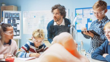 İlköğretim Okulu Kimya Sınıfı: Coşkulu Öğretmen, Beher 'de kimyasalları karıştırıp köpük fil diş macunu kullandıkları için çeşitli çocuk gruplarına bilim reaksiyon deneyleri öğretiyor 