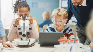 İlköğretim Okulu Bilim Sınıfı: Şirin Küçük Kız Mikroskop Altında Bakıyor, Çocuk İnternet 'teki bilgileri kontrol etmek için Dijital Tablet Bilgisayar kullanıyor, Hevesli Öğretmen Ders Açıklıyor