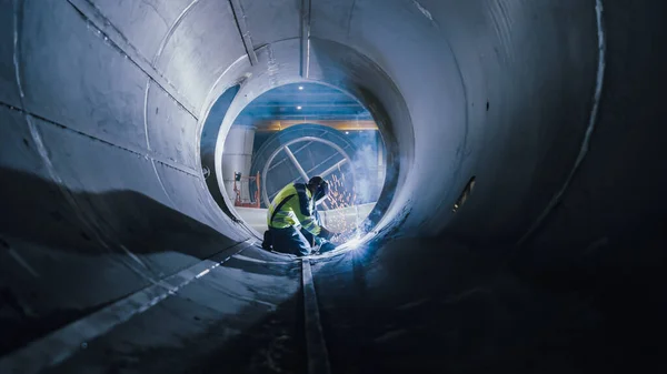 Professioneller Schweißer aus der Schwerindustrie, der im Rohr arbeitet, trägt Helm und beginnt zu schweißen. Bau der Transportpipeline für Öl, Erdgas und Treibstoffe. Fabrik für industrielle Fertigung — Stockfoto