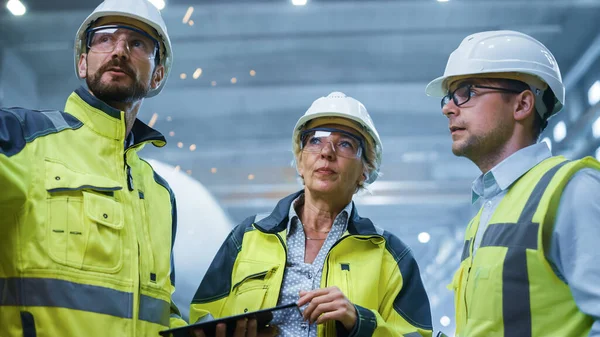 Three Heavy Industry Engineers Stand in Pipe Manufacturing Factory, Use Digital Tablet Computer, Have Discussion. Large Pipe Assembly. Design and Construction of Oil, Gas and Fuels Transport Pipeline — Stock Photo, Image