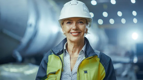 专业重工业女工程师身穿安全制服,头戴硬帽,笑容可亲的画像.在焊接火花飞扬的大工业厂房背景下 — 图库照片