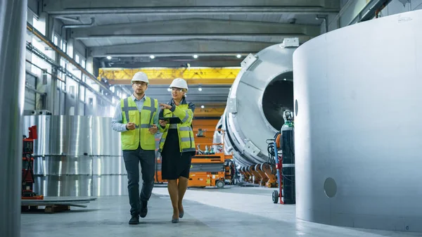 Zwei Ingenieure der Schwerindustrie gehen durch die Fabrik zur Rohrherstellung, benutzen digitale Tablet-Computer, diskutieren. Fazilität für den Bau von Öl-, Gas- und Kraftstoffpipelines. — Stockfoto