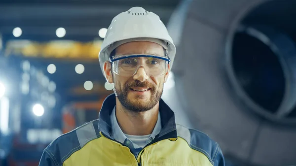 Porträt eines lächelnden, professionellen Schwerindustrie-Ingenieurs, der Sicherheitsuniform, Brille und Hut trägt. Im Hintergrund unkonzentrierte große Industriefabrik — Stockfoto