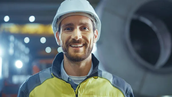 Porträt eines lächelnden, professionellen Schwerindustrie-Ingenieurs, der Sicherheitsuniform und Hut trägt. Im Hintergrund unkonzentrierte große Industriefabrik — Stockfoto