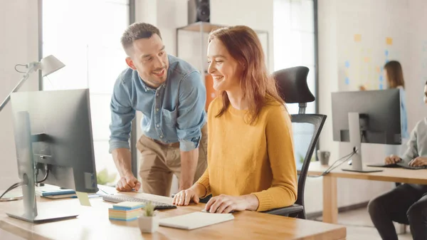 Especialista femenina trabaja en la computadora de escritorio, Project Manager se queda al lado y da consejos sobre la optimización del flujo de trabajo para la gestión de la experiencia del cliente. Oficina moderna con equipo diverso de profesionales — Foto de Stock