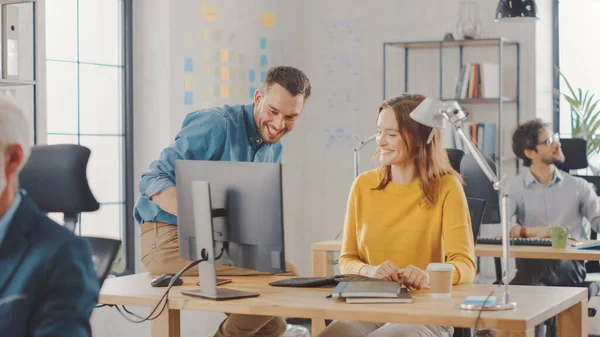 Spécialiste féminine travaille sur ordinateur de bureau, chef de projet se tient à côté et donne des conseils sur l'optimisation du flux de travail pour la gestion de l'expérience client. Bureau moderne avec une équipe diversifiée de professionnels — Photo